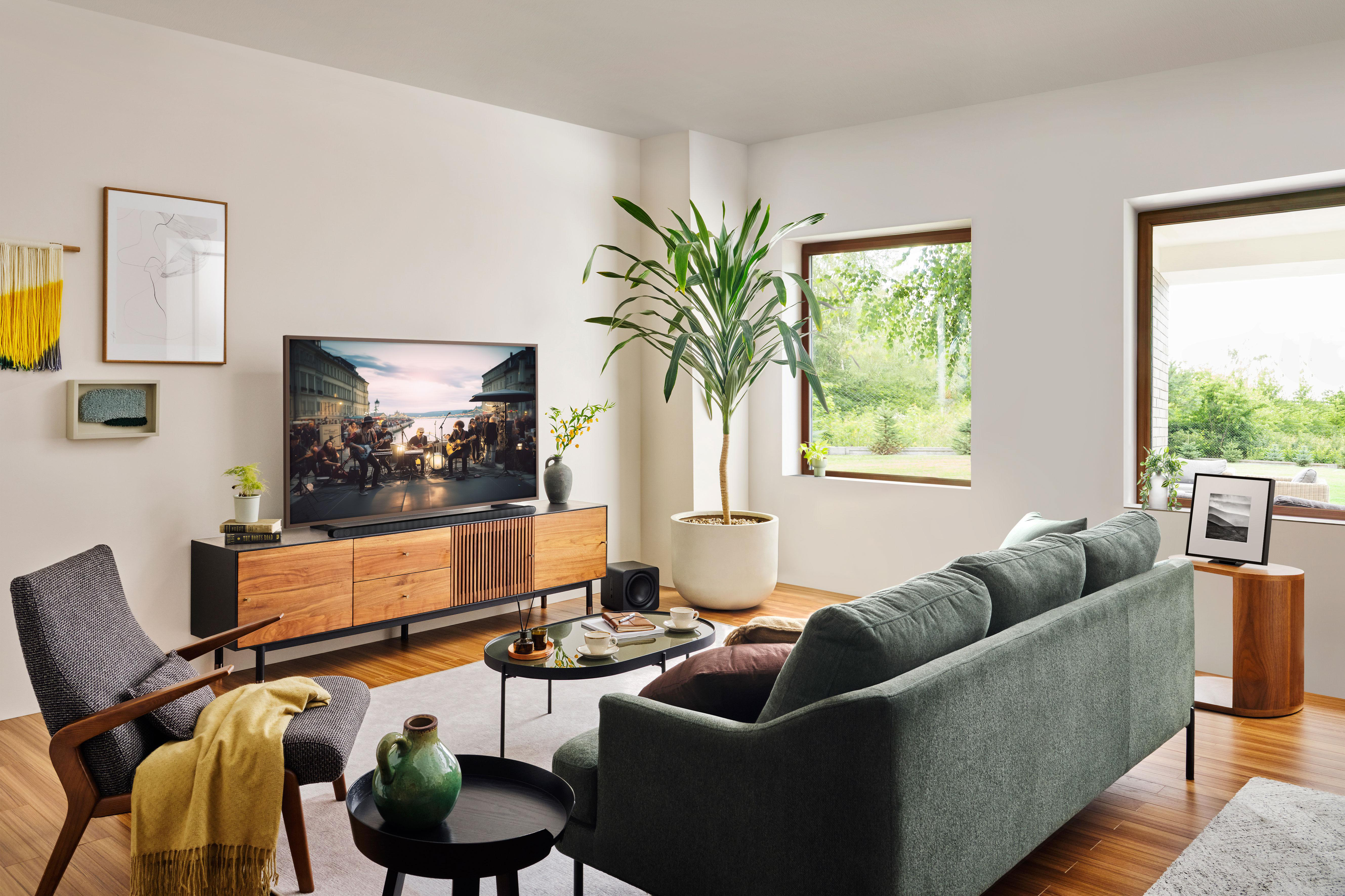 Wohnzimmer mit Fernseher, Holzmöbeln, Sofa, Pflanze und Fenster. Gut beleuchtet.