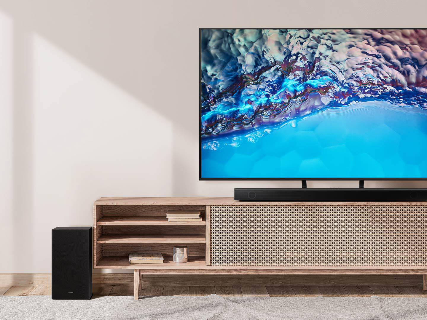 Wohnzimmer mit Fernseher, Soundbar und Subwoofer. Heller Holzschrank und Teppich.