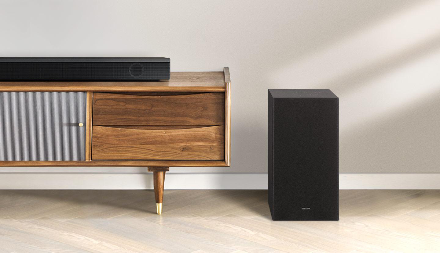 Eine schwarze Soundbar und ein Subwoofer auf einem Holzschrank, in einem Raum mit weißer Wand.
