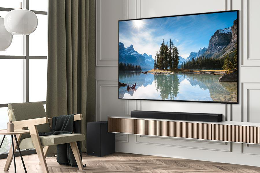 Ein Wohnzimmer mit TV, der eine Berglandschaft zeigt, Soundbar und schwarzem Subwoofer.