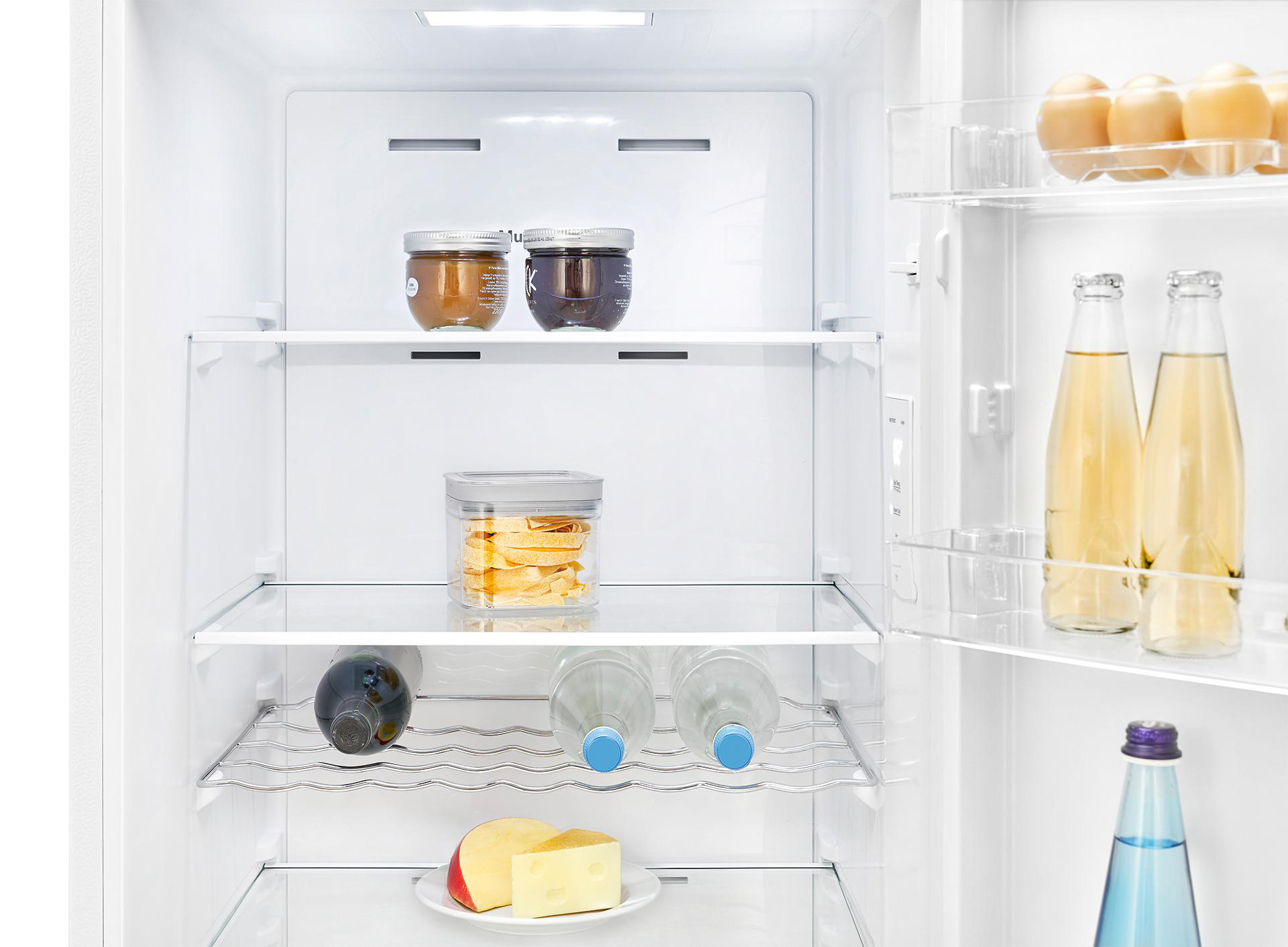 Offener Kühlschrank mit Regalen, die Gläser, Flaschen, einen Käseteller und Obst enthalten.