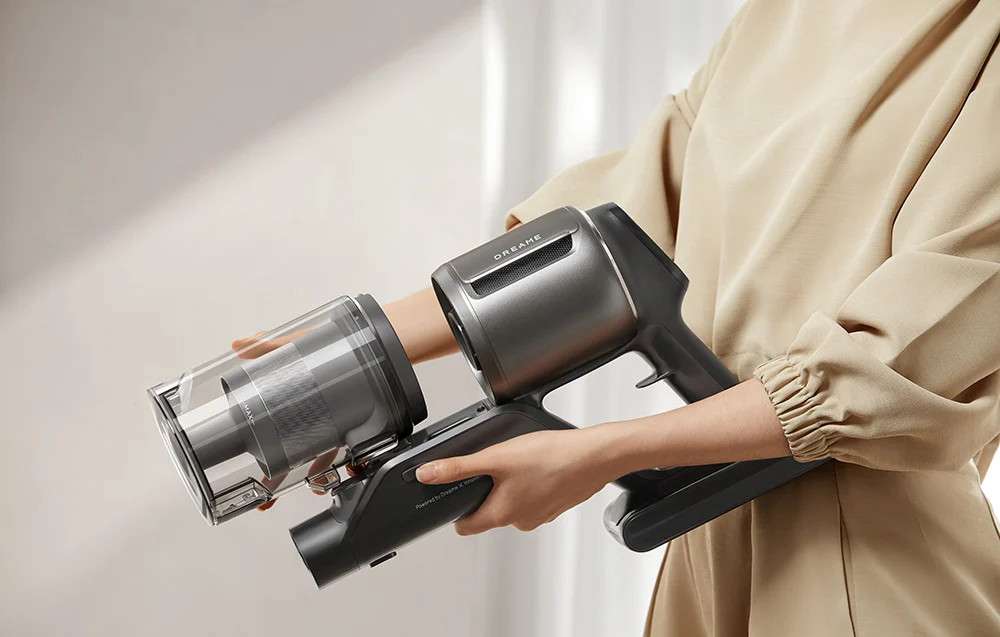 Osoba trzymająca srebrno-czarny odkurzacz. Jest on trzymany na wysokości klatki piersiowej.