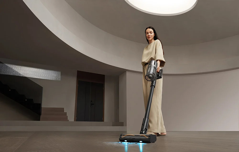 Kobieta odkurza jasną podłogę. Odkurzacz jest czarny i szary.