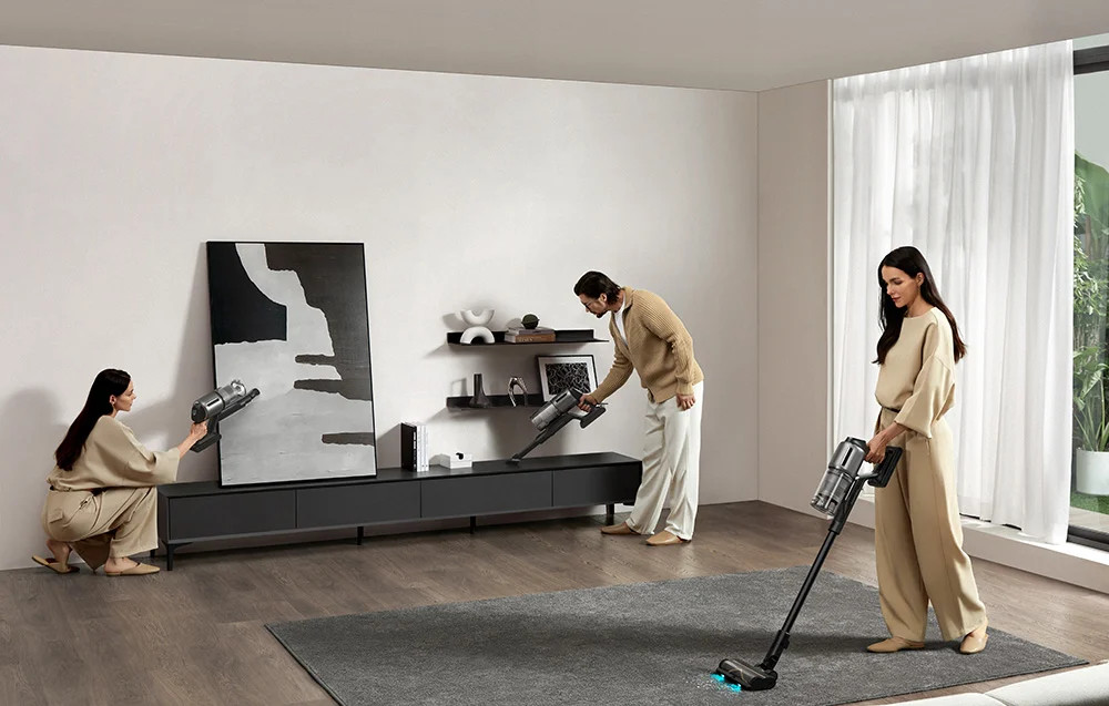 Trzy osoby sprzątają pokój za pomocą odkurzaczy, jedna używa mopa i dzieła sztuki.