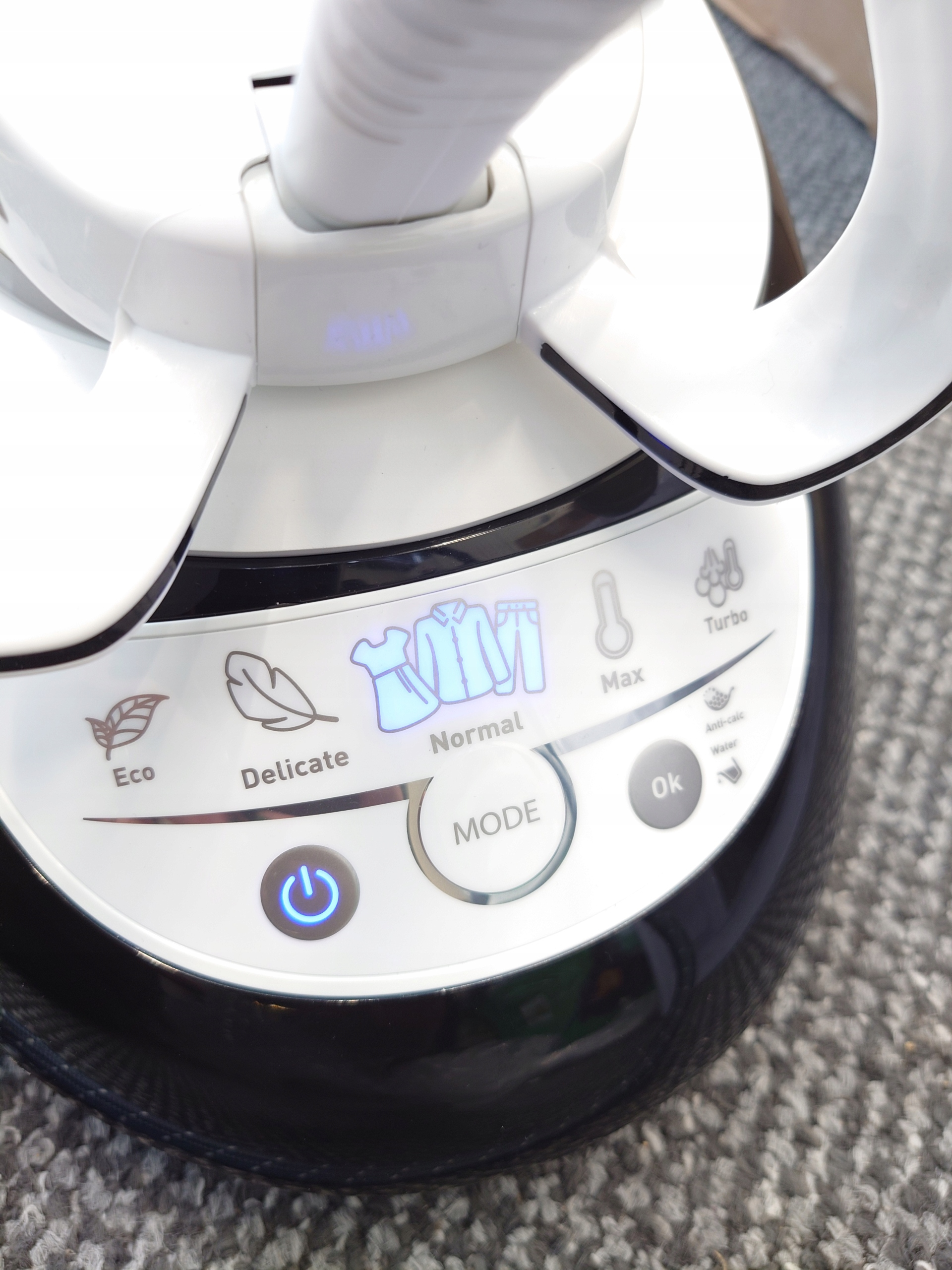 Zbliżenie białego panelu sterowania parownicy z ikonami i przyciskiem zasilania.