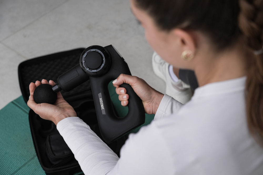 Woman holding a black massage gun with a black case open nearby.