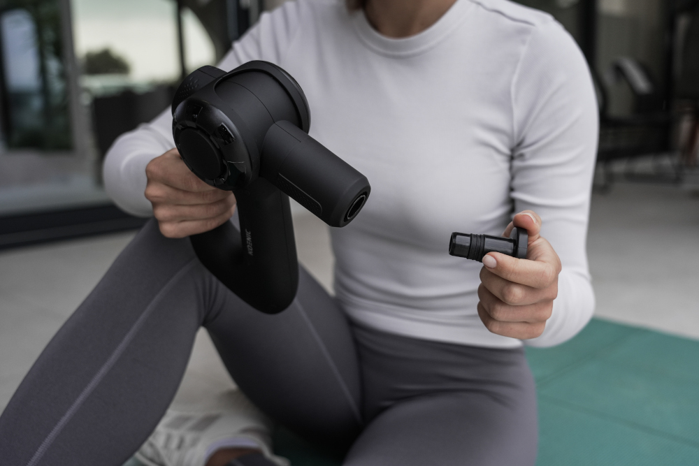 A woman sits holding a black massage device and attachment.