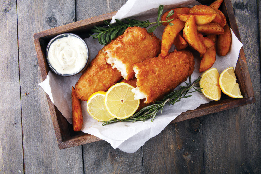Fish and chips with lemon slices and sauce in a wooden tray. Rosemary is also present.