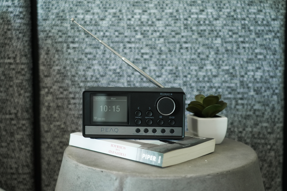 A black radio with a digital clock sits on a small table. A plant and book are beside it.