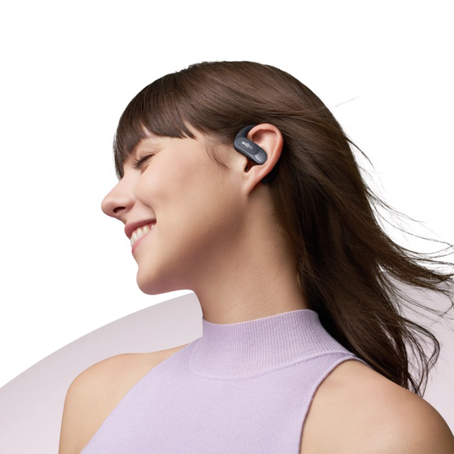 Donna sorridente con un auricolare wireless. Top lilla chiaro. Sfondo chiaro.