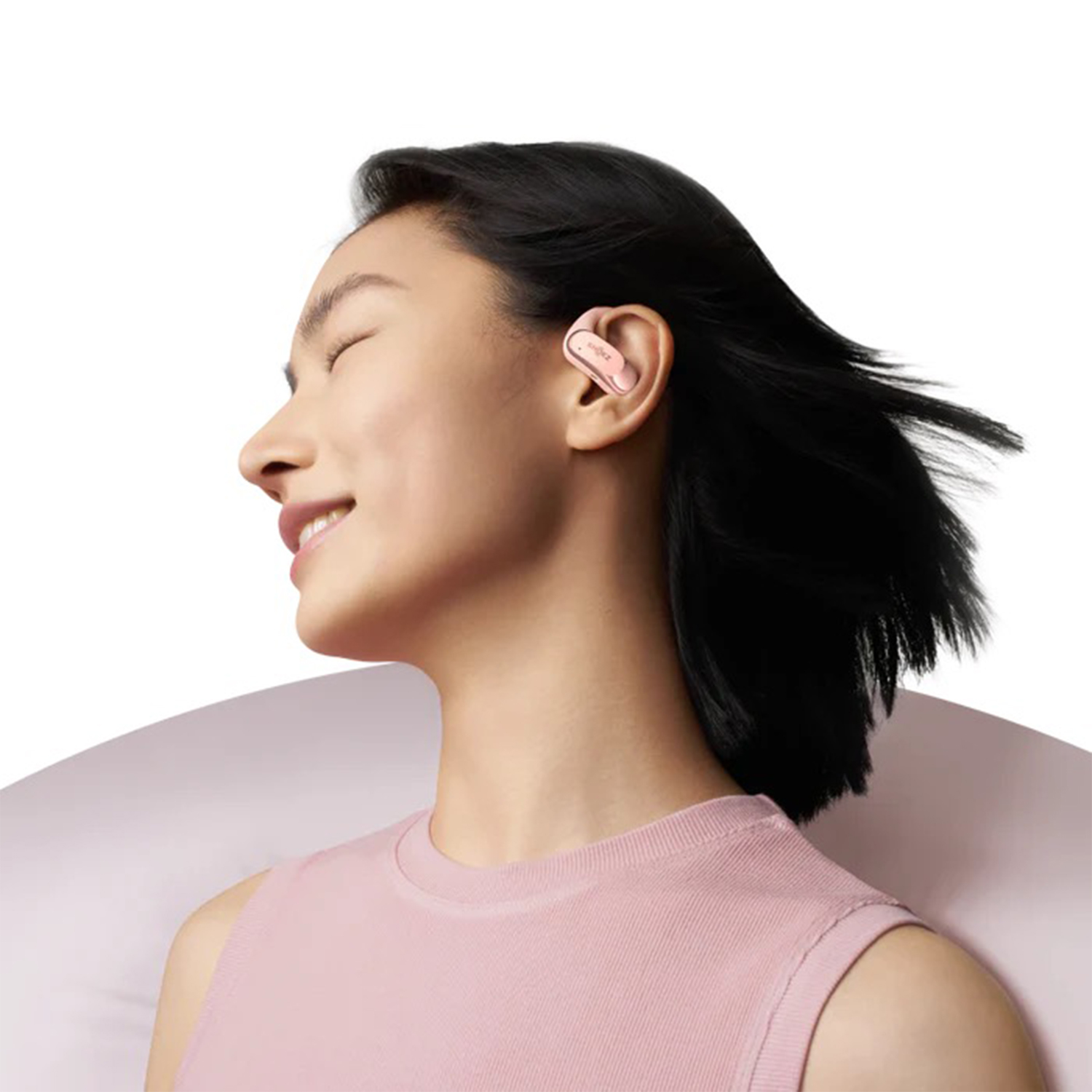 Donna con auricolari rosa nell'orecchio, sorridente con gli occhi chiusi.