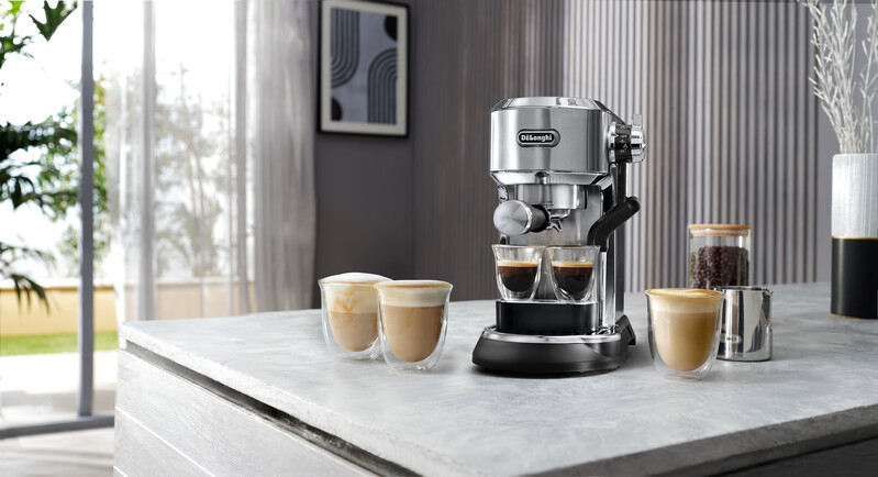 Espresso machine with two coffees. Bean jar and a vase on a marble countertop. Kitchen setting.