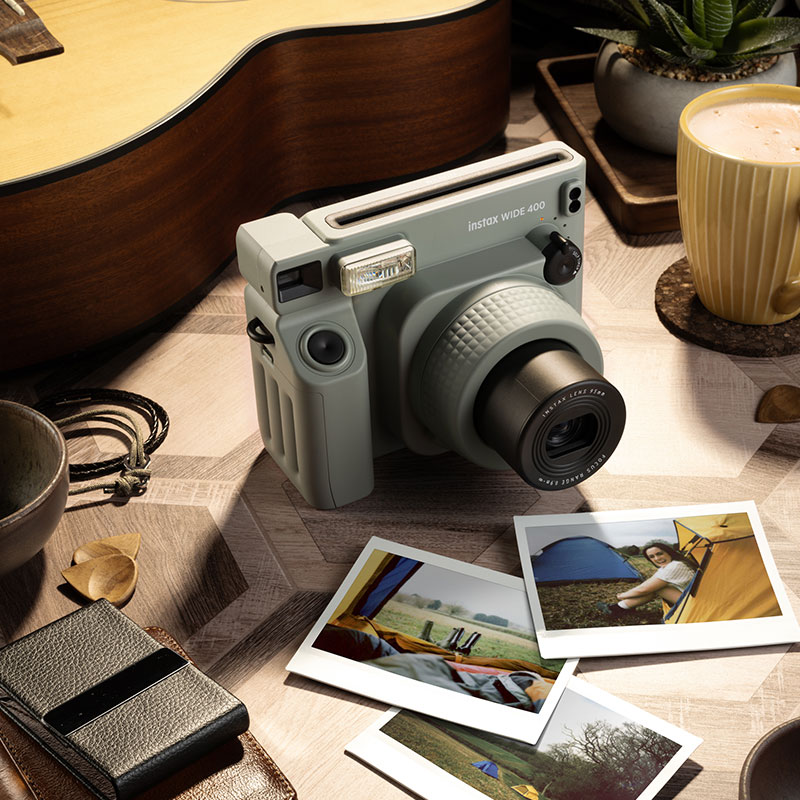 Instax Wide 400 Kamera, Fotos und Gitarre auf einem Holztisch mit verschiedenen Gegenständen.