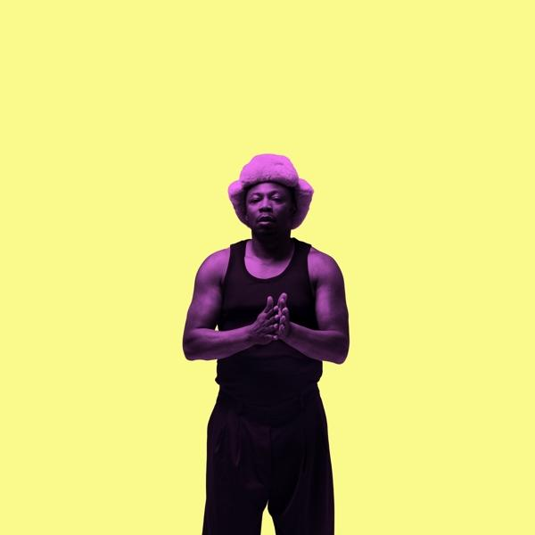 Homme avec chapeau violet et débardeur noir sur fond jaune. Mains jointes.