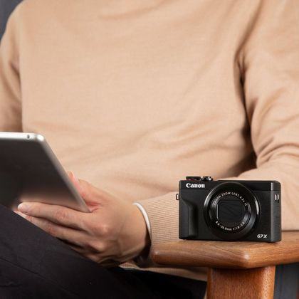 Eine Person hält ein Tablet und eine schwarze Kamera. Sie sitzen auf einem Stuhl.
