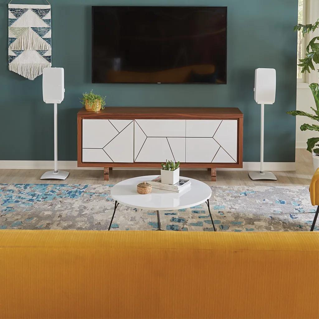 Ein Wohnzimmer mit Fernseher, Sideboard, Couch, Teppich und Lautsprechern.