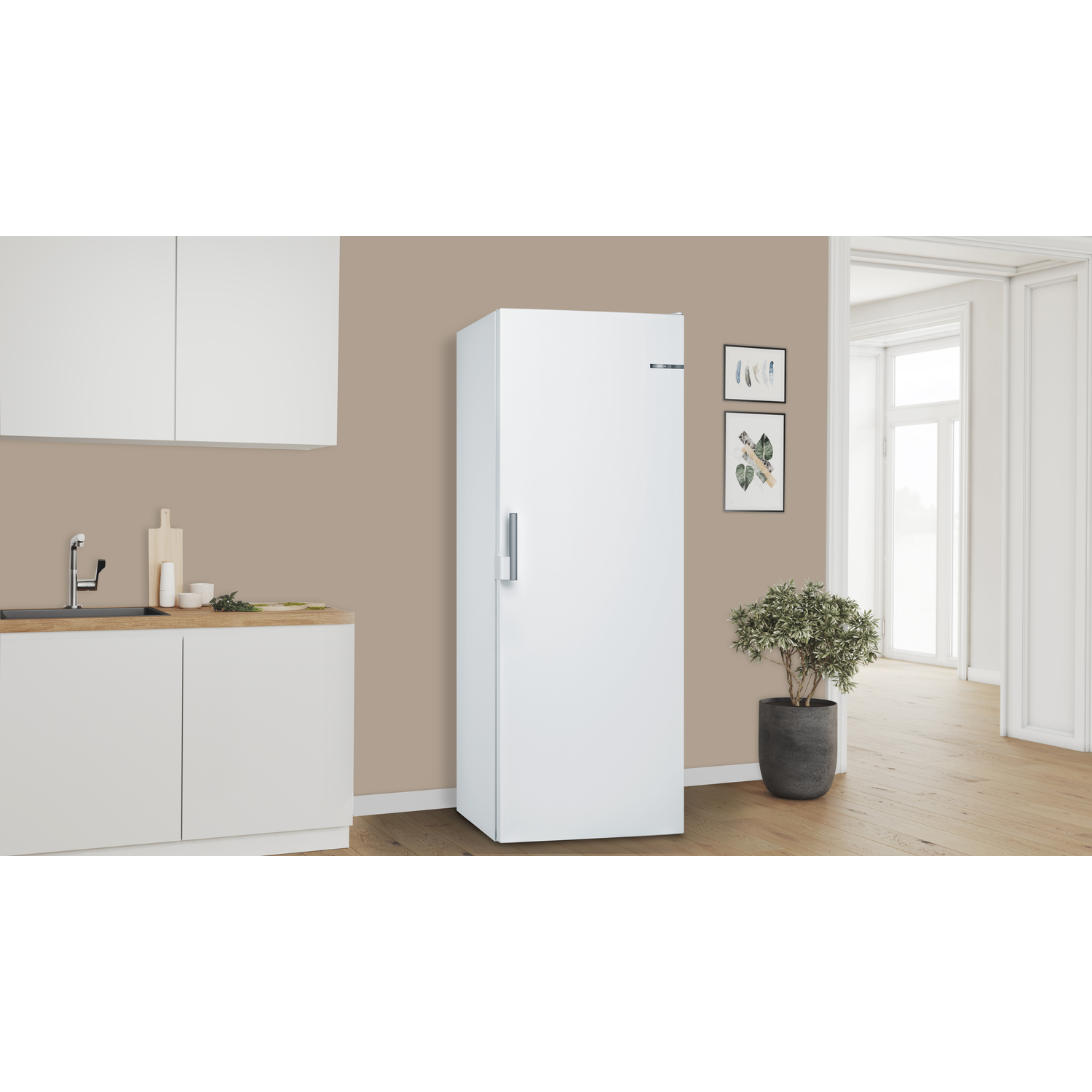 Witte vrijstaande koelkast in een keuken. Beige muur, houten aanrecht en plant in pot.