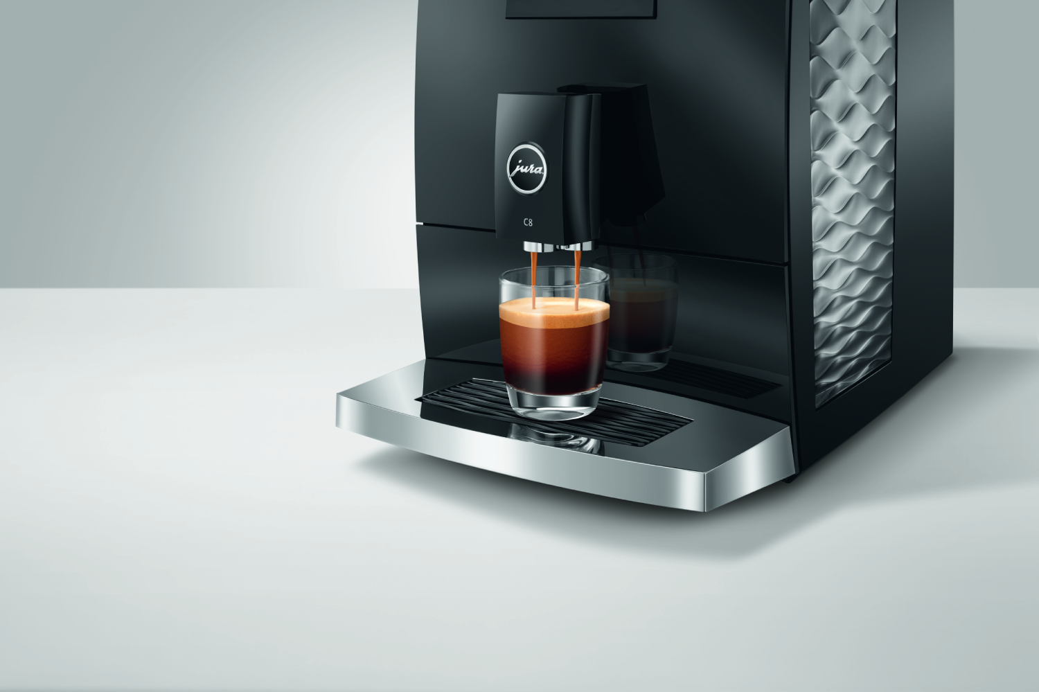 Máquina de espresso Jura C8 negra. Espresso vertiéndose en un vaso. Superficie blanca, fondo claro.