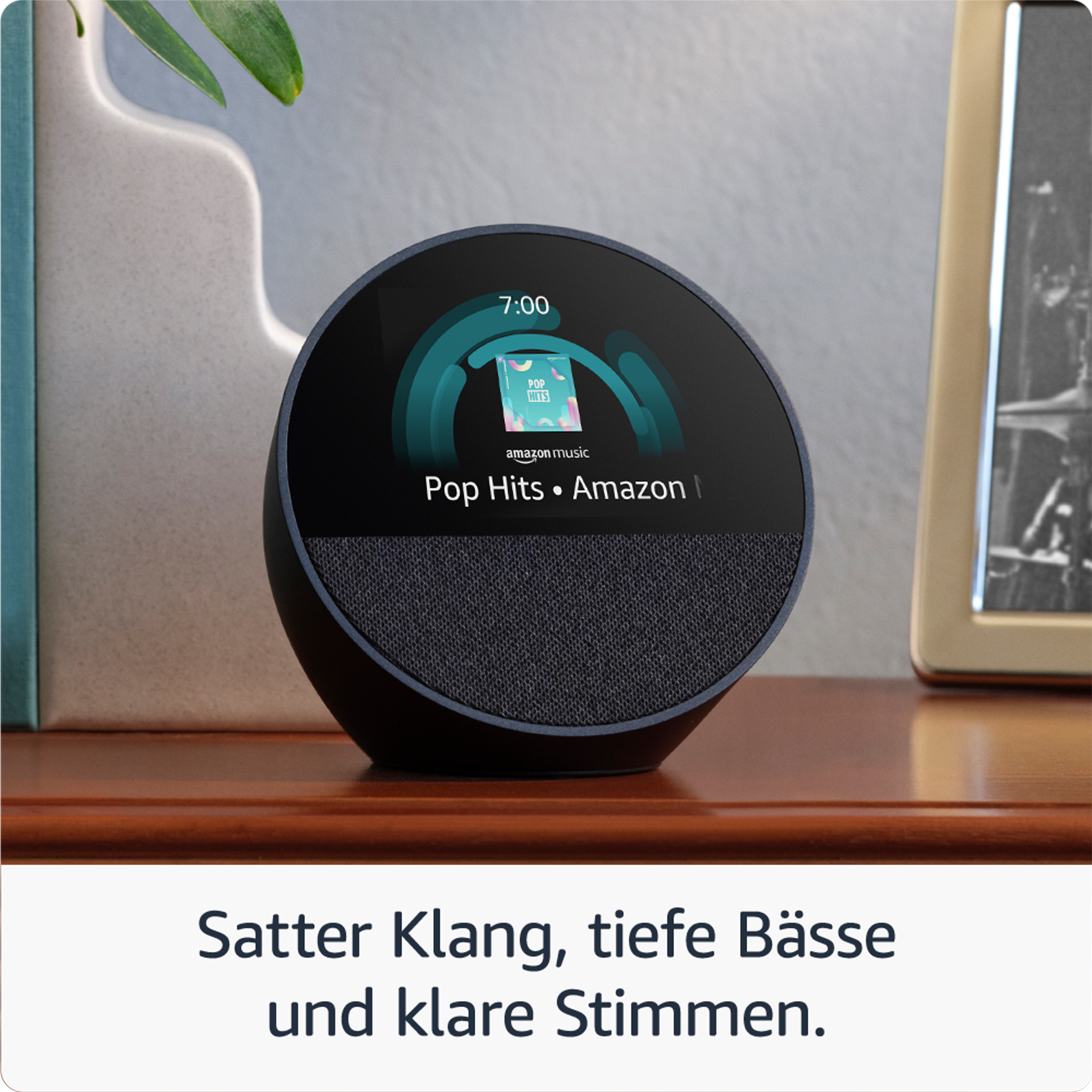 Schwarzer Smart-Lautsprecher mit Bildschirm, zeigt eine Musik-App. Hintergrund: Holztisch, Dekoration.