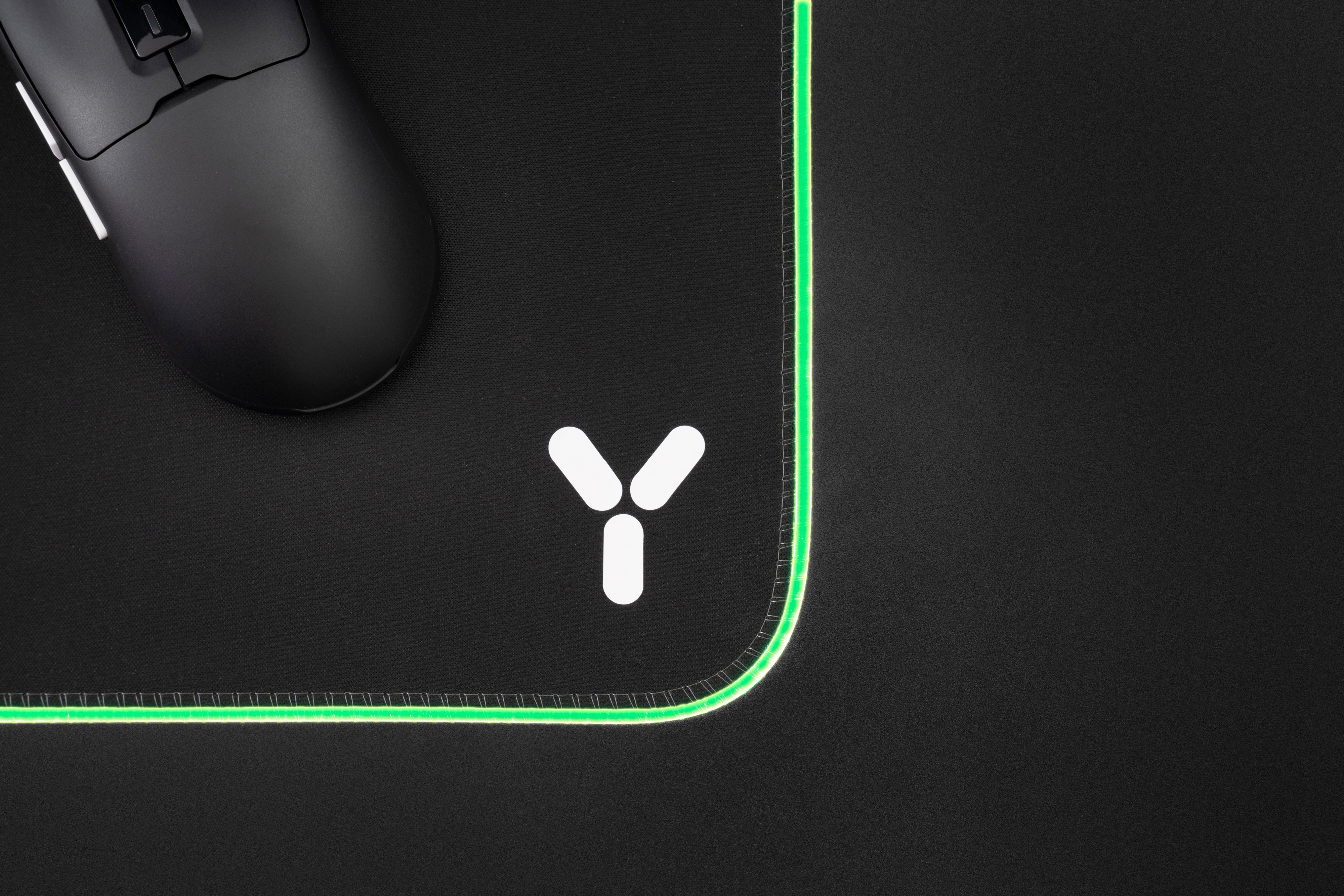 Schwarze Gaming-Maus auf schwarzem Mauspad mit weißem Logo und grünem Rand.