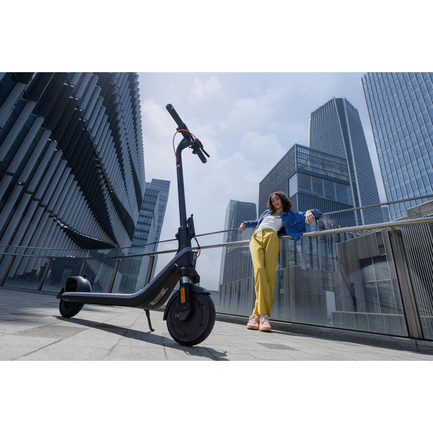 Persoon leunt op een reling naast een e-scooter in een moderne stedelijke omgeving.