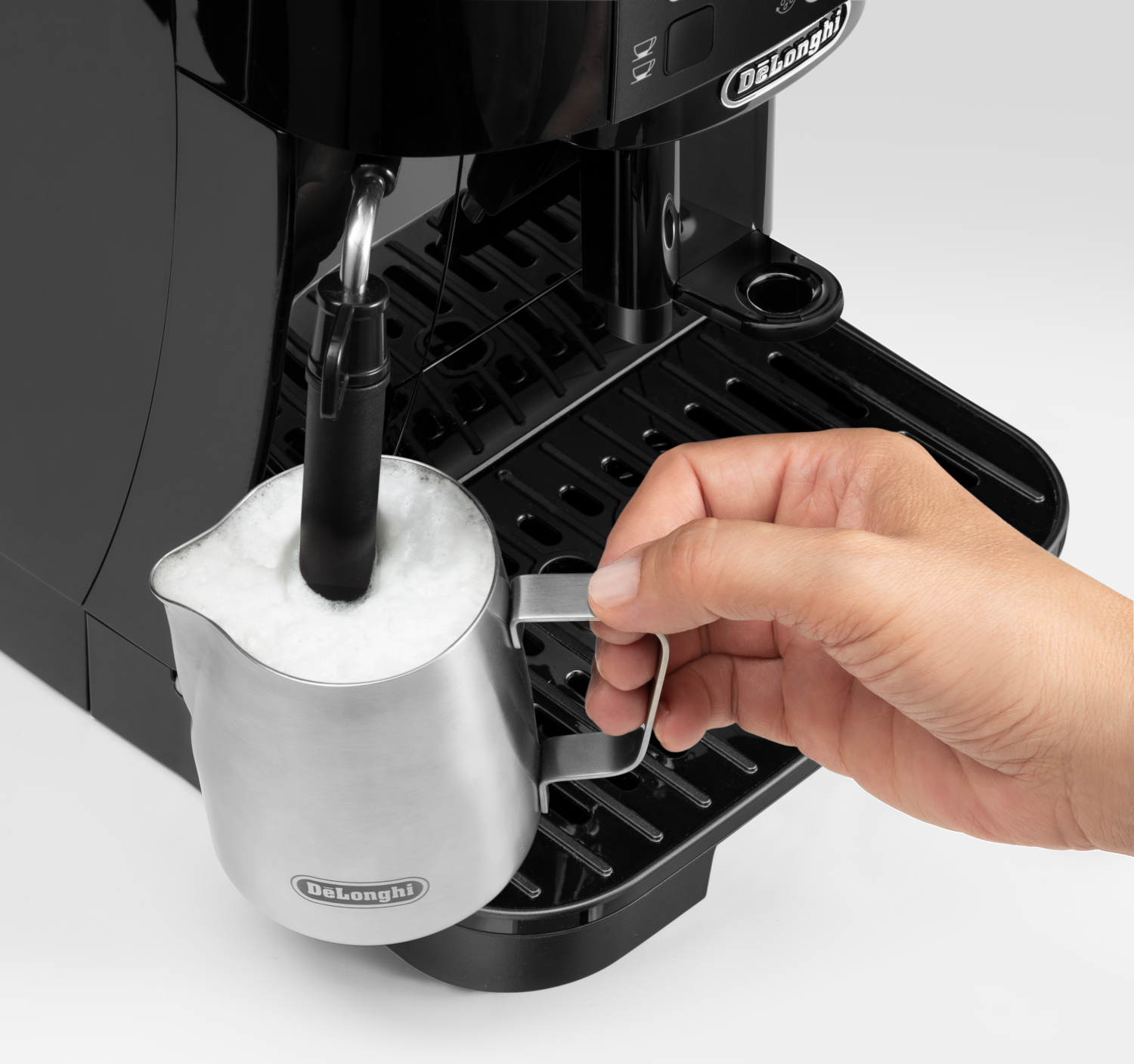 Egy kéz tejhabot készít egy Delonghi eszpresszó géppel.