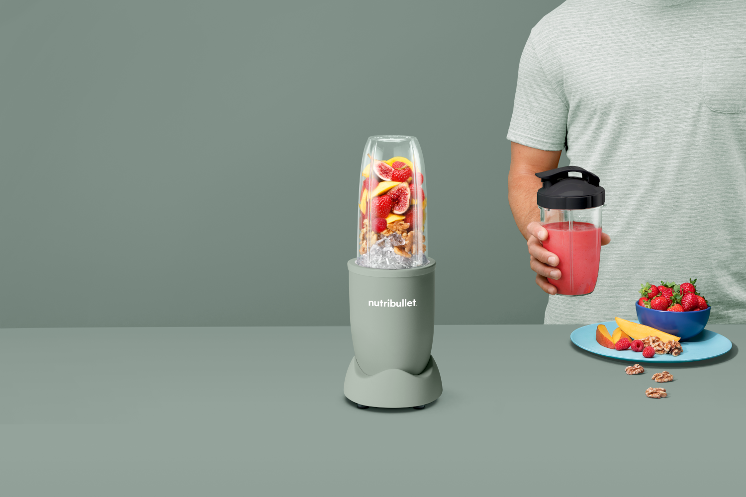 Turmixgép gyümölccsel. Férfi shake-et, gyümölcsöt és diót tart az asztalon.