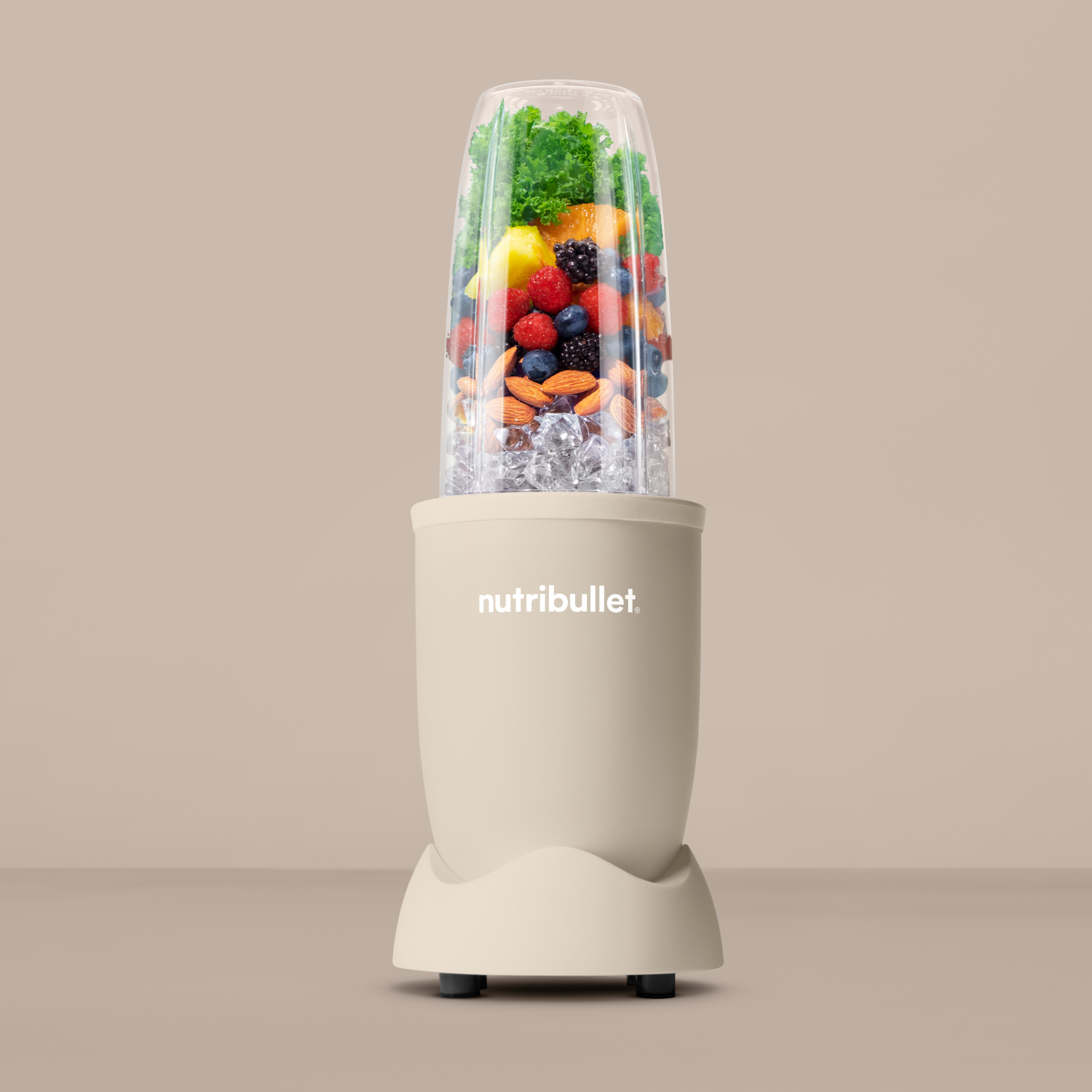 Egy bézs Nutribullet turmixgép gyümölcsökkel, jéggel és zöldségekkel töltve, bézs háttér előtt.