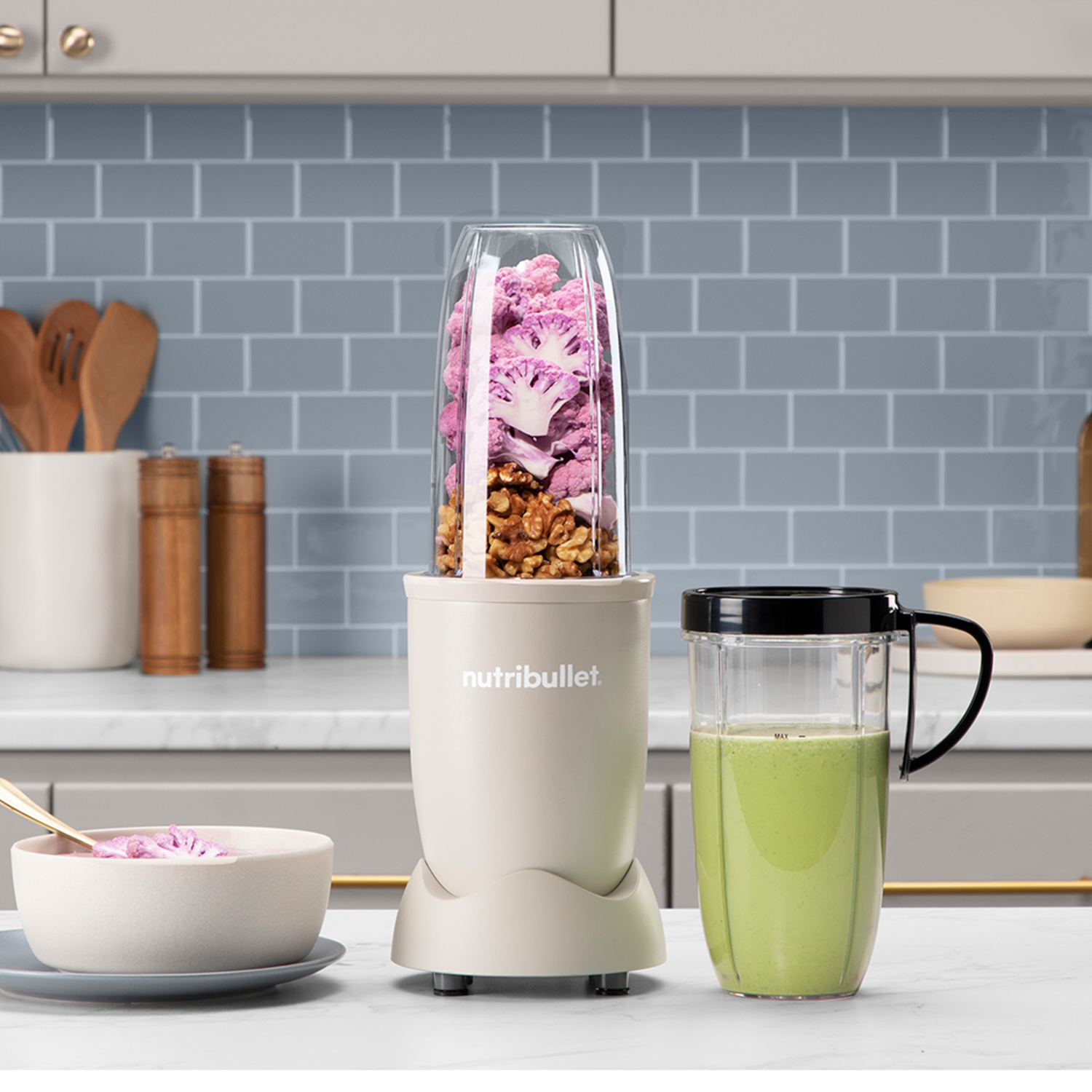 Turmixgép hozzávalókkal. Lila karfiol és dió belül. Egy zöld smoothie mellette.