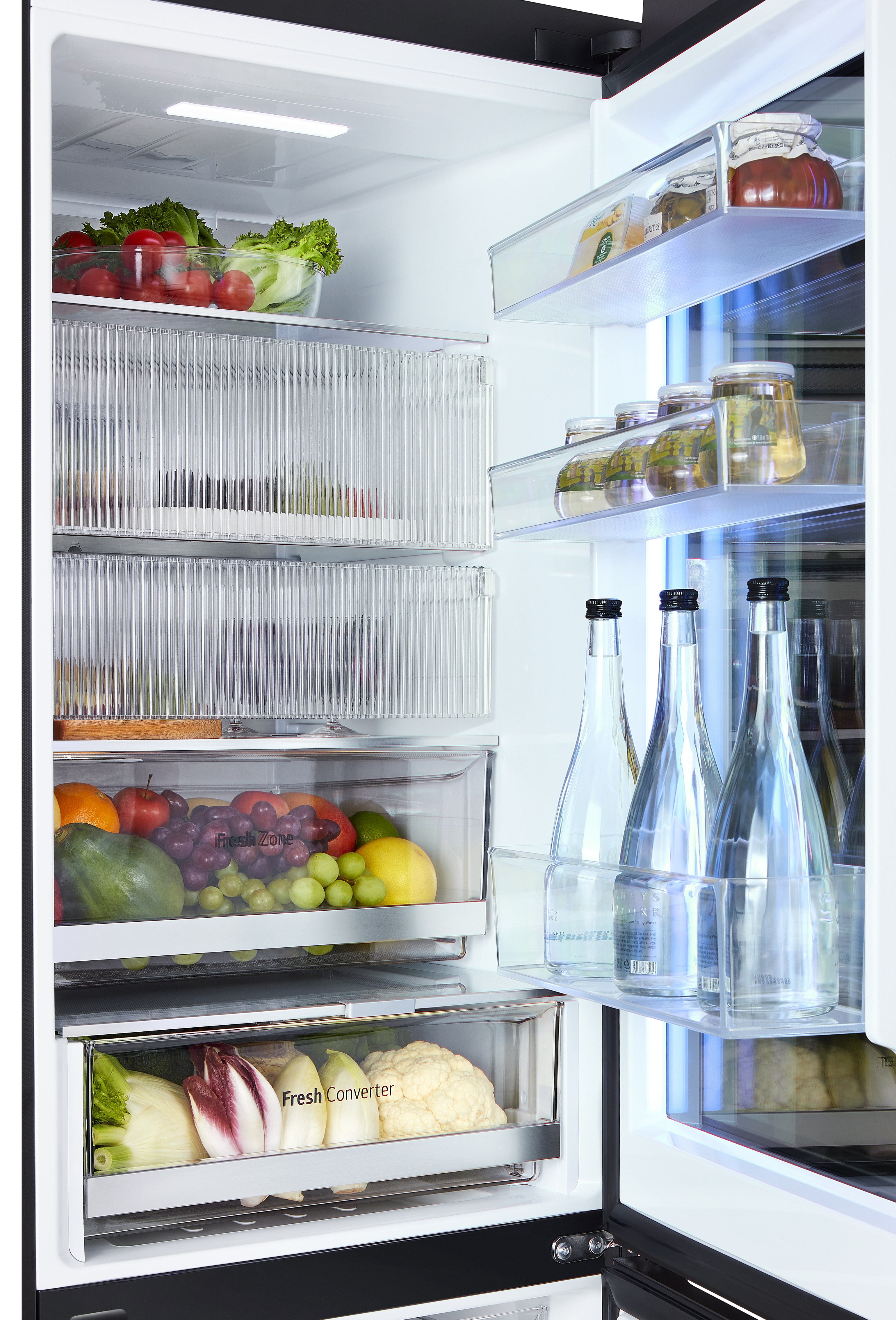 Otwarta lodówka z półkami z owocami, warzywami i butelkami.