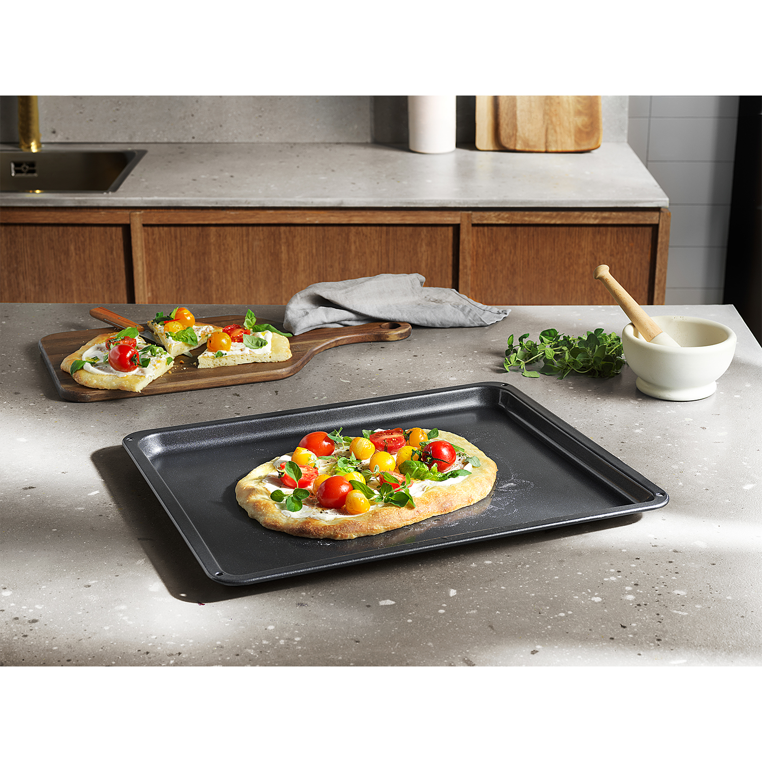Pizza su una teglia. Ingredienti: pomodori e basilico. Piano di lavoro grigio, tagliere in legno.