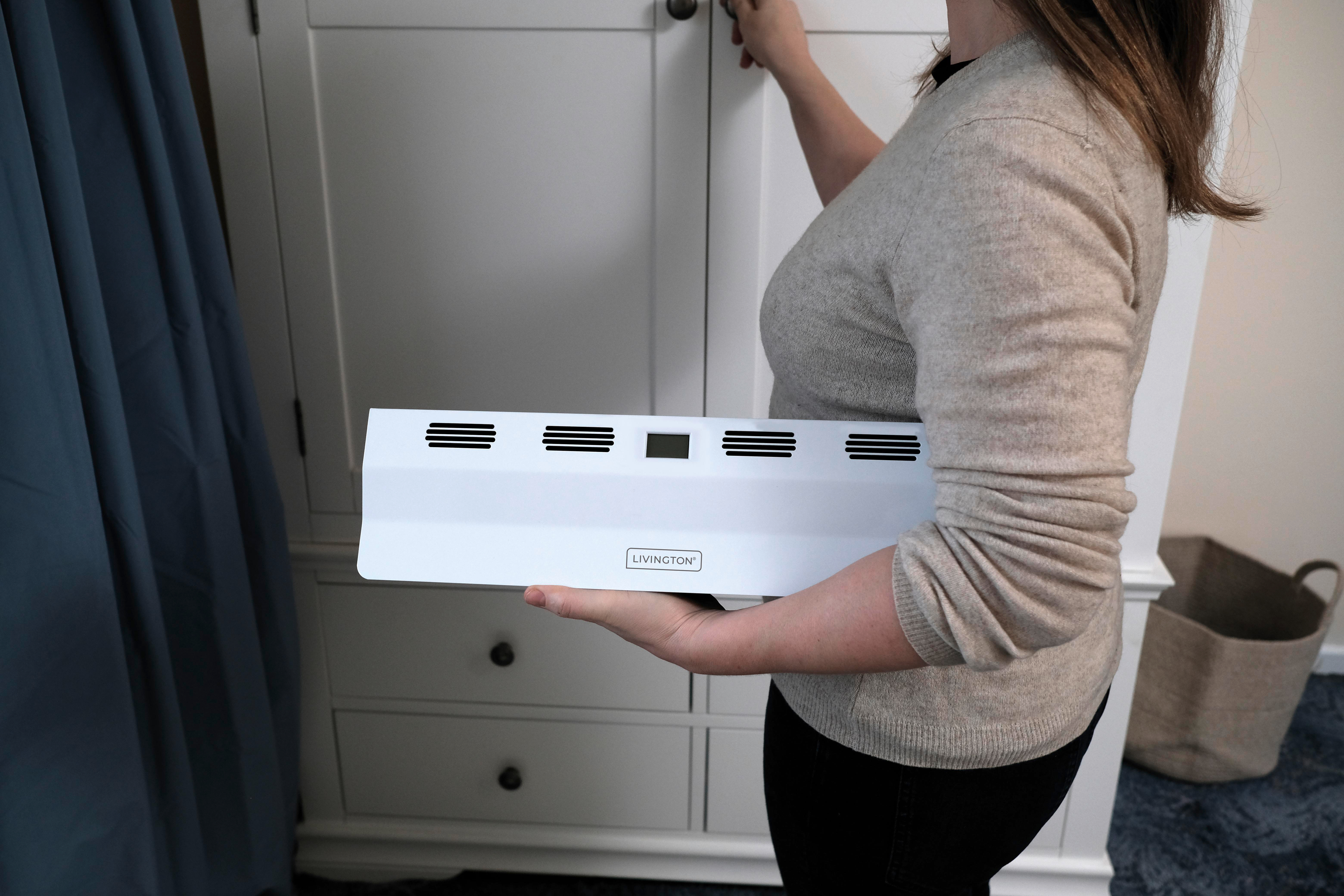 Person hält eine weiße Livingston-Heizung und platziert sie in einem Schrank.