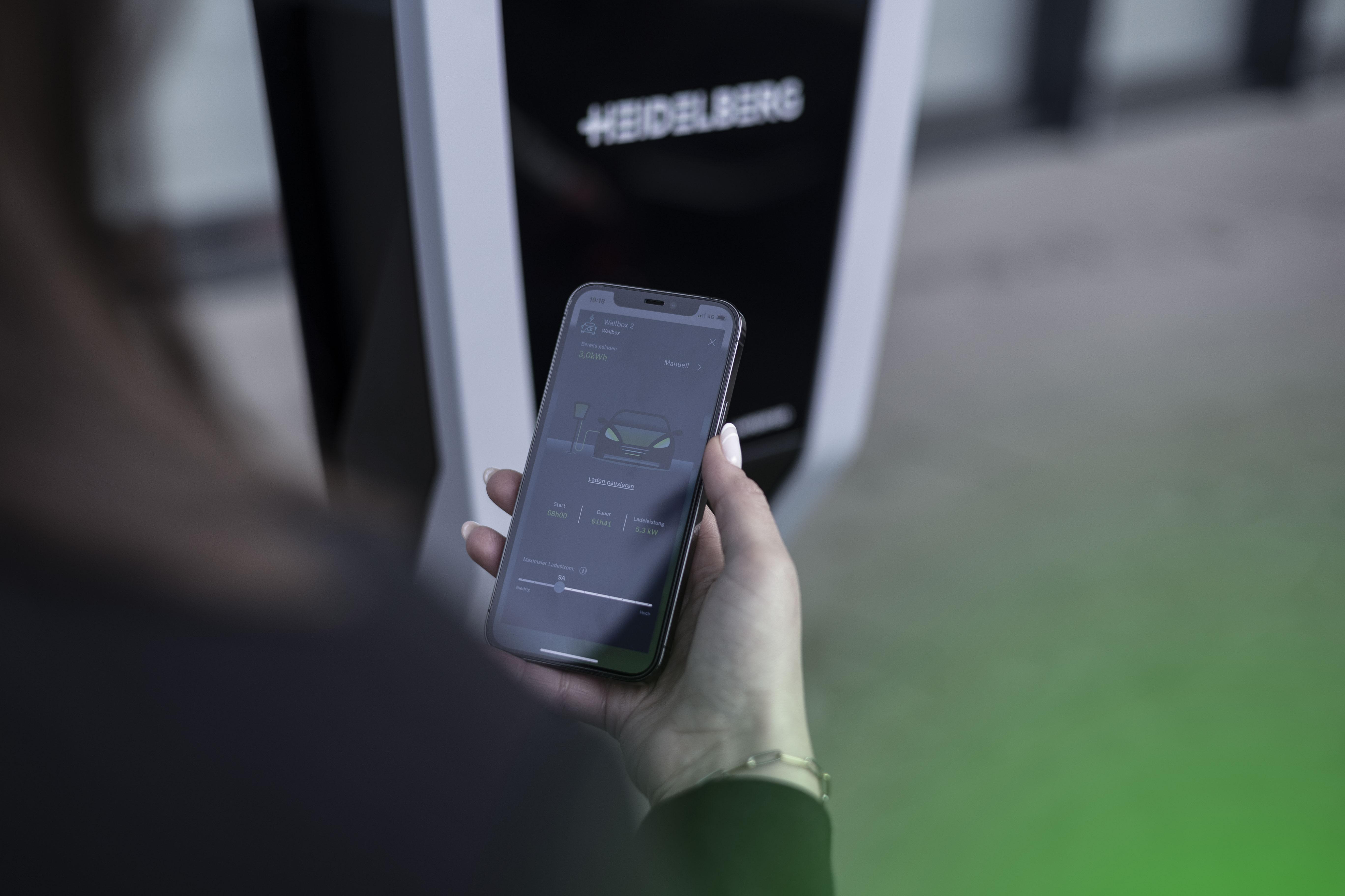 Eine Person steuert eine Ladestation mit einem Smartphone.