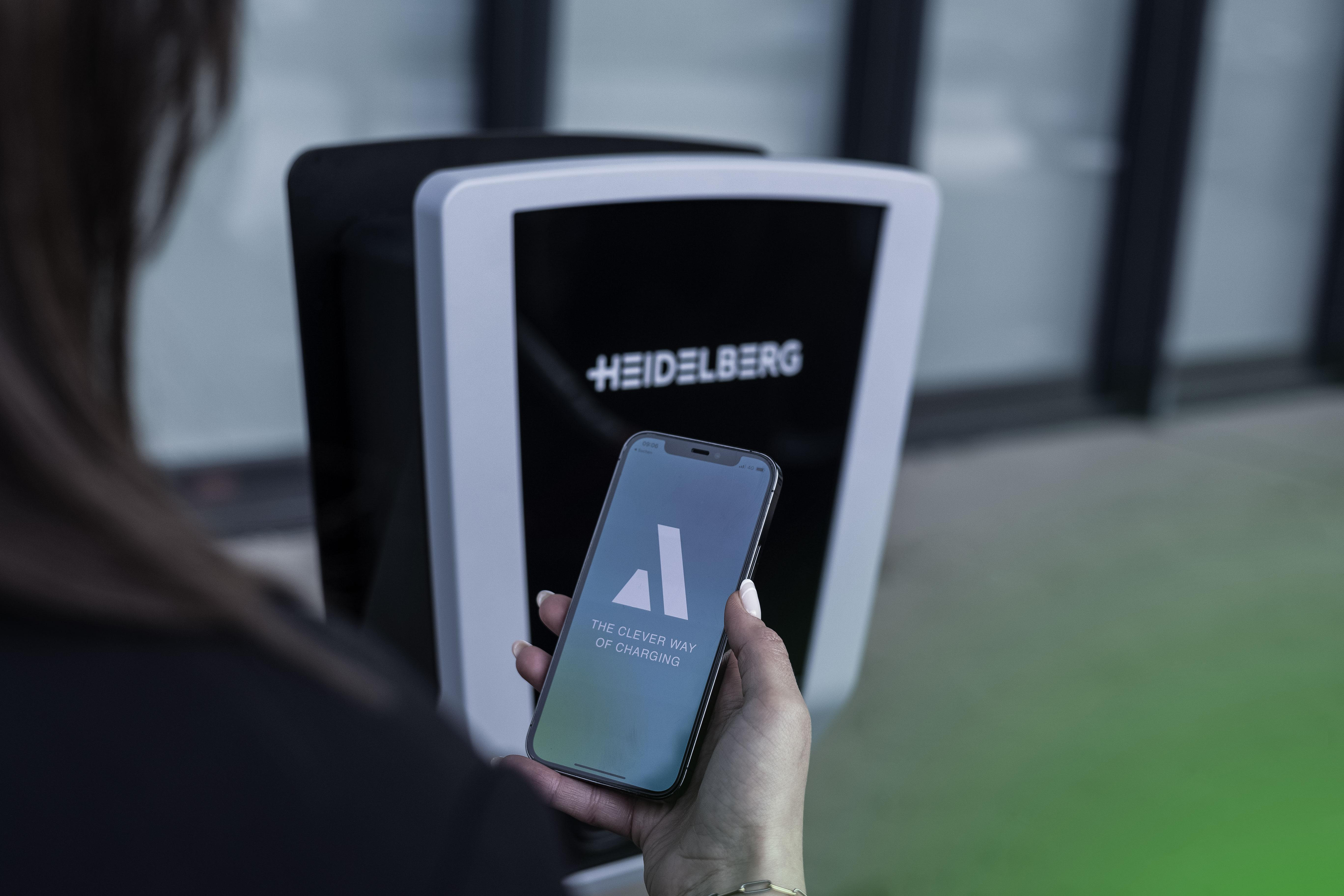 Eine Person hält ein Telefon in der Nähe einer Heidelberg-Ladestation.