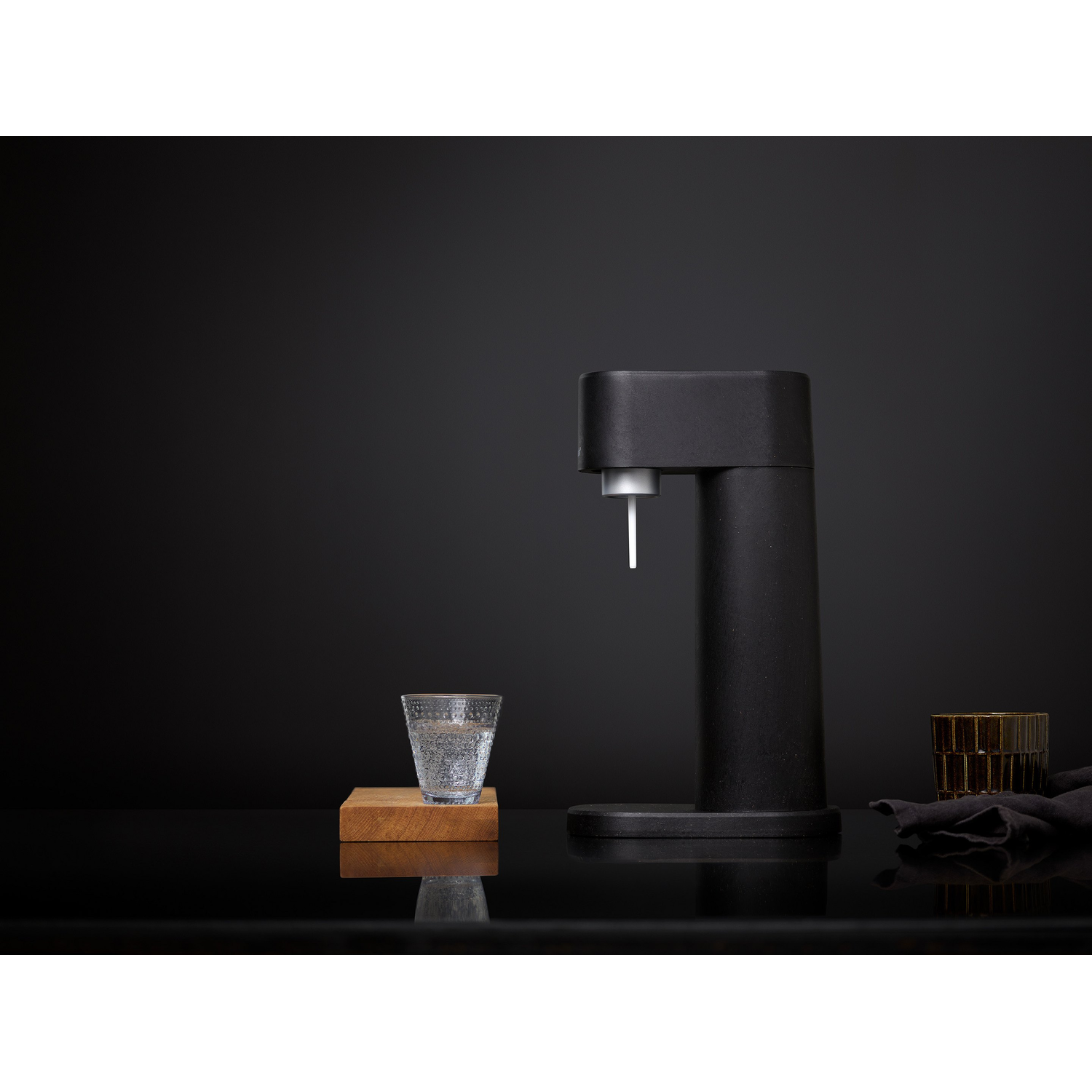Zwarte sodamaker, glas water op een houten blok, zwarte achtergrond.