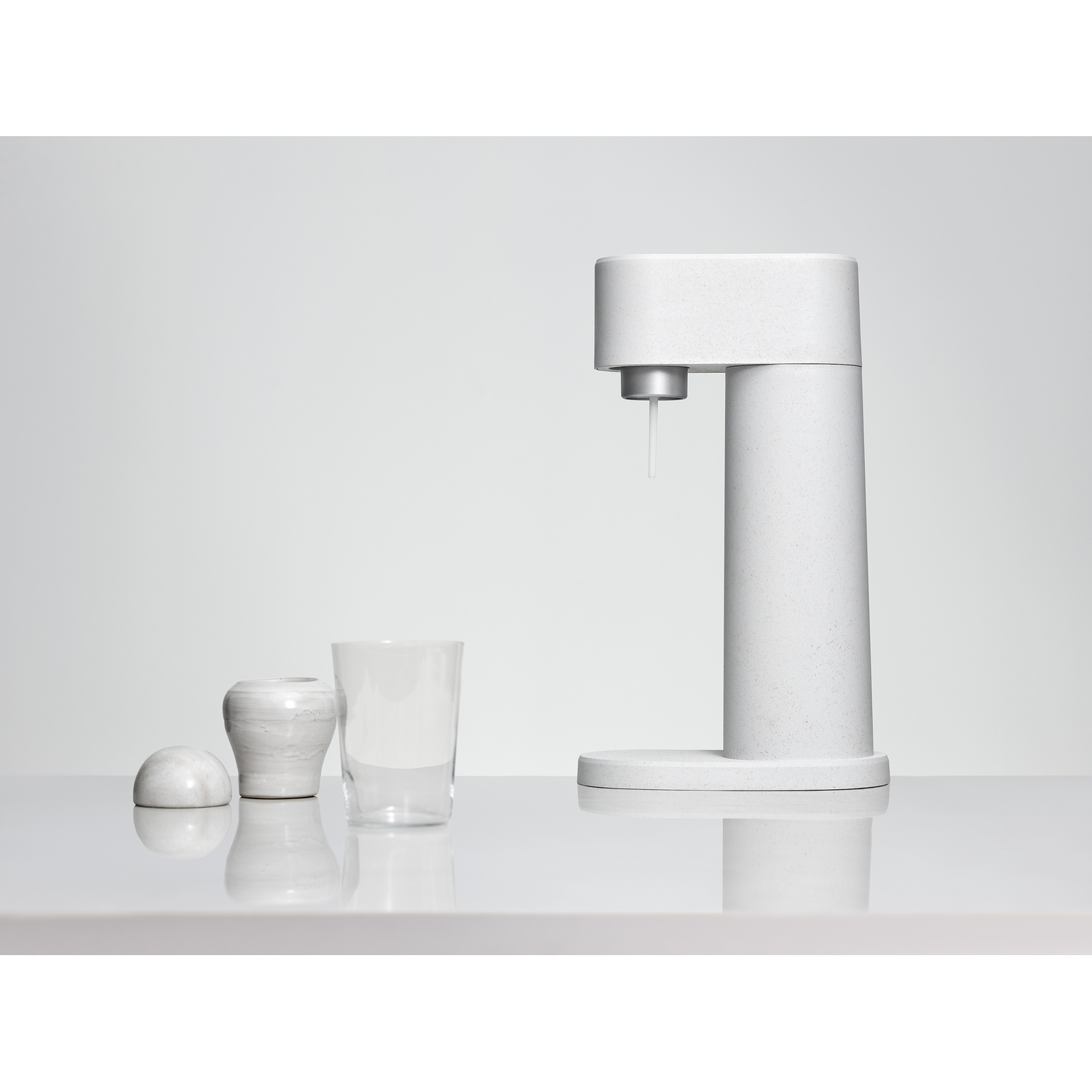 Een witte sodamaker met een glas en twee kleine vazen op een wit oppervlak. Het ontwerp is modern en strak.