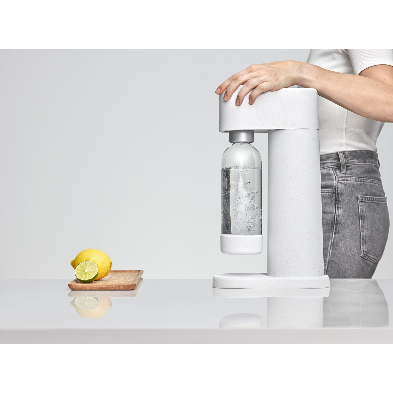 Een witte SodaStream-machine met een waterfles, een citroen en de hand van een vrouw.