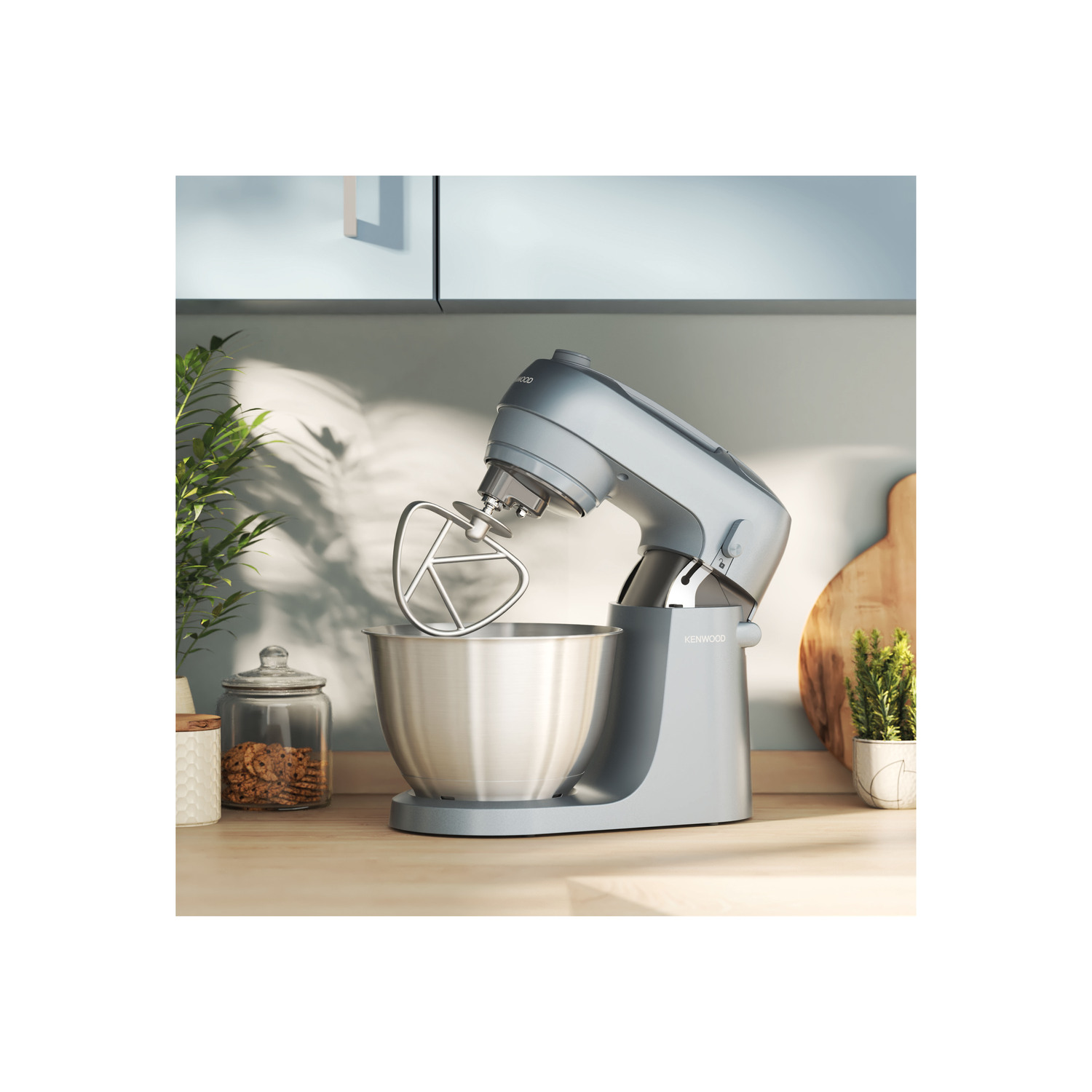 A gray stand mixer with a mixing attachment in a stainless steel bowl, in a kitchen setting.
