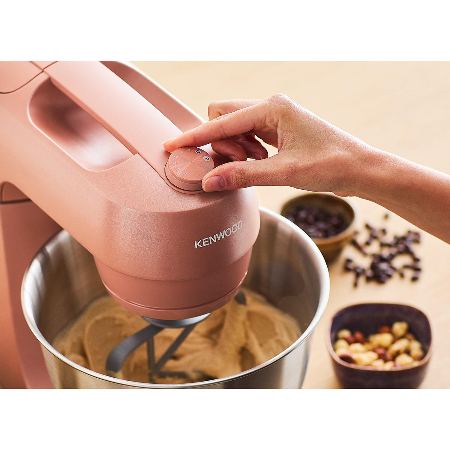 Person using a Kenwood mixer. A bowl with dough, and ingredients in bowls are near.
