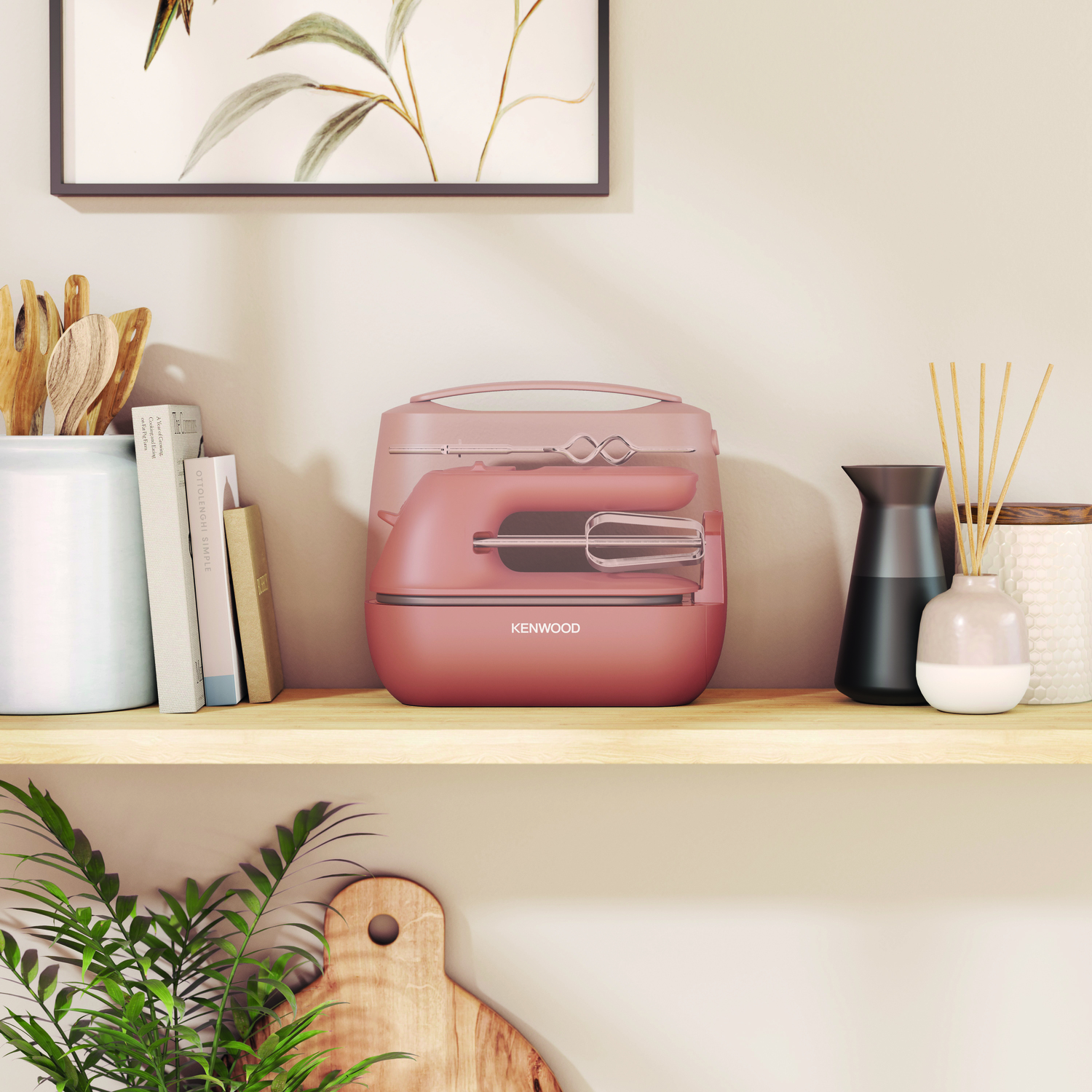 A pink hand mixer in its case, on a shelf with decor, a plant, and a cutting board.