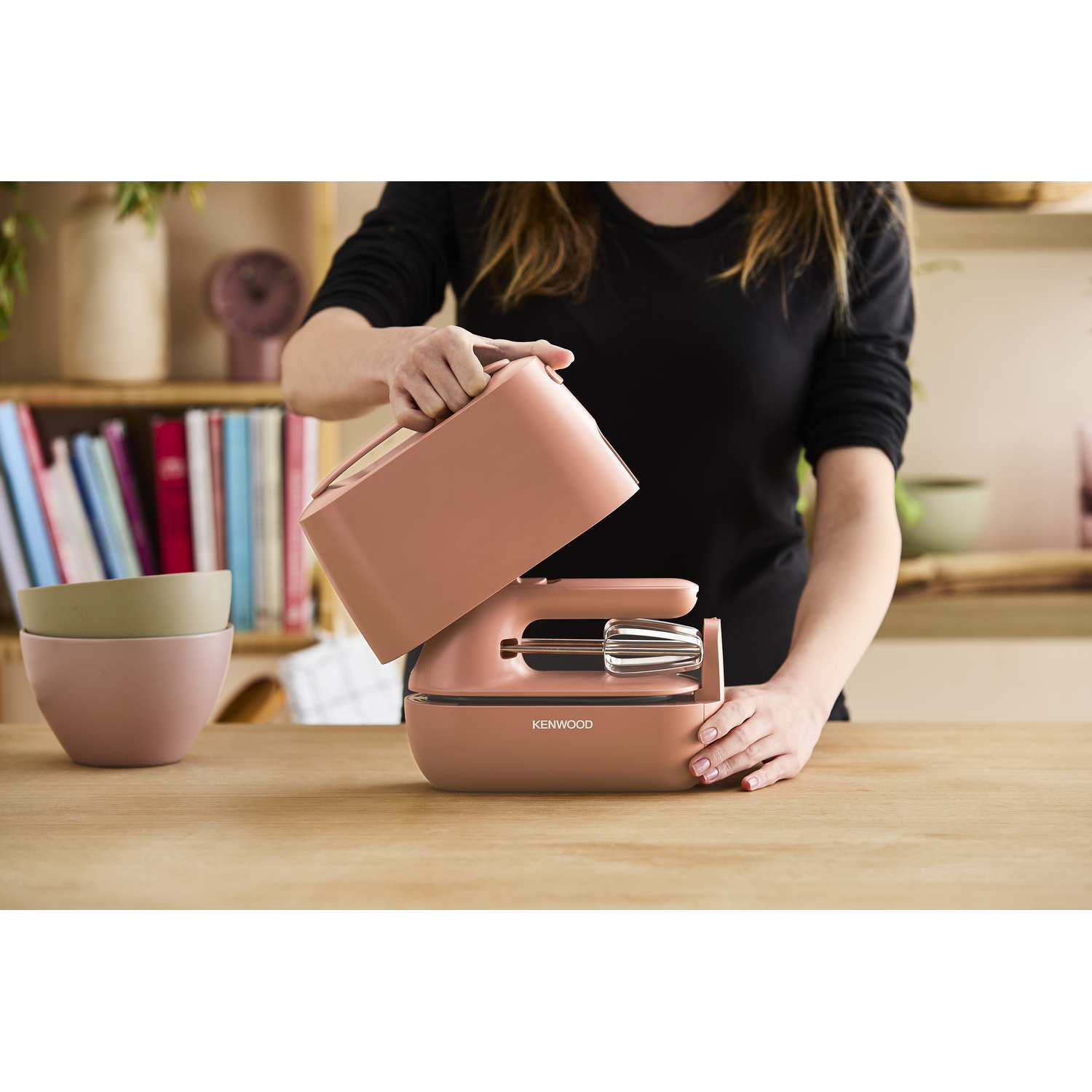 Woman holding a pink mixer above a mixer base and bowls.