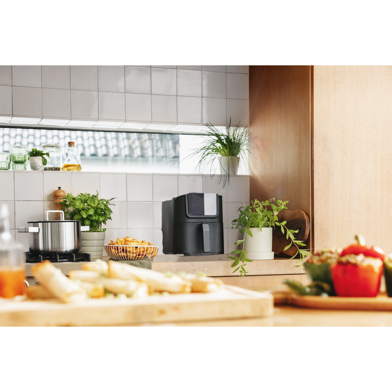 Kitchen scene with air fryer, food, plants, and cooking utensils. Focus is on the air fryer.