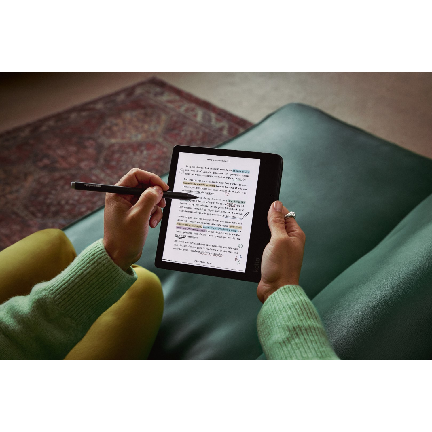 A person using a Kobo e-reader with a stylus, on a green couch.