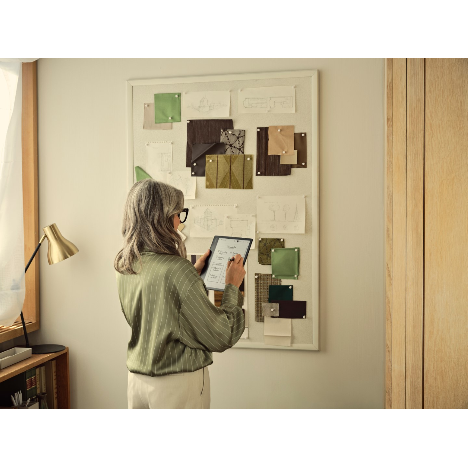 Woman looking at tablet with drawings on a wall, wearing glasses.