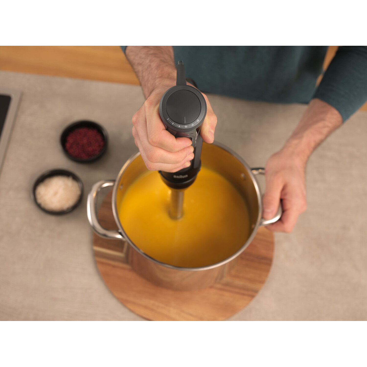 A person's hand holding an immersion blender, blending soup in a pot.