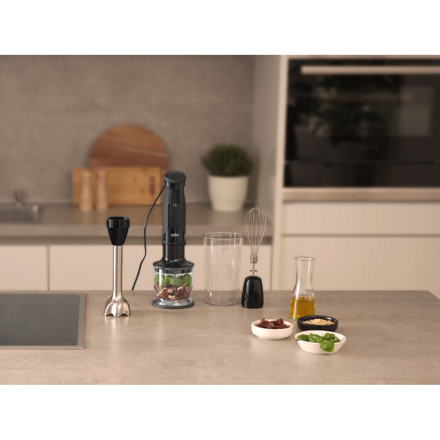 A hand blender with accessories and ingredients on a kitchen counter.