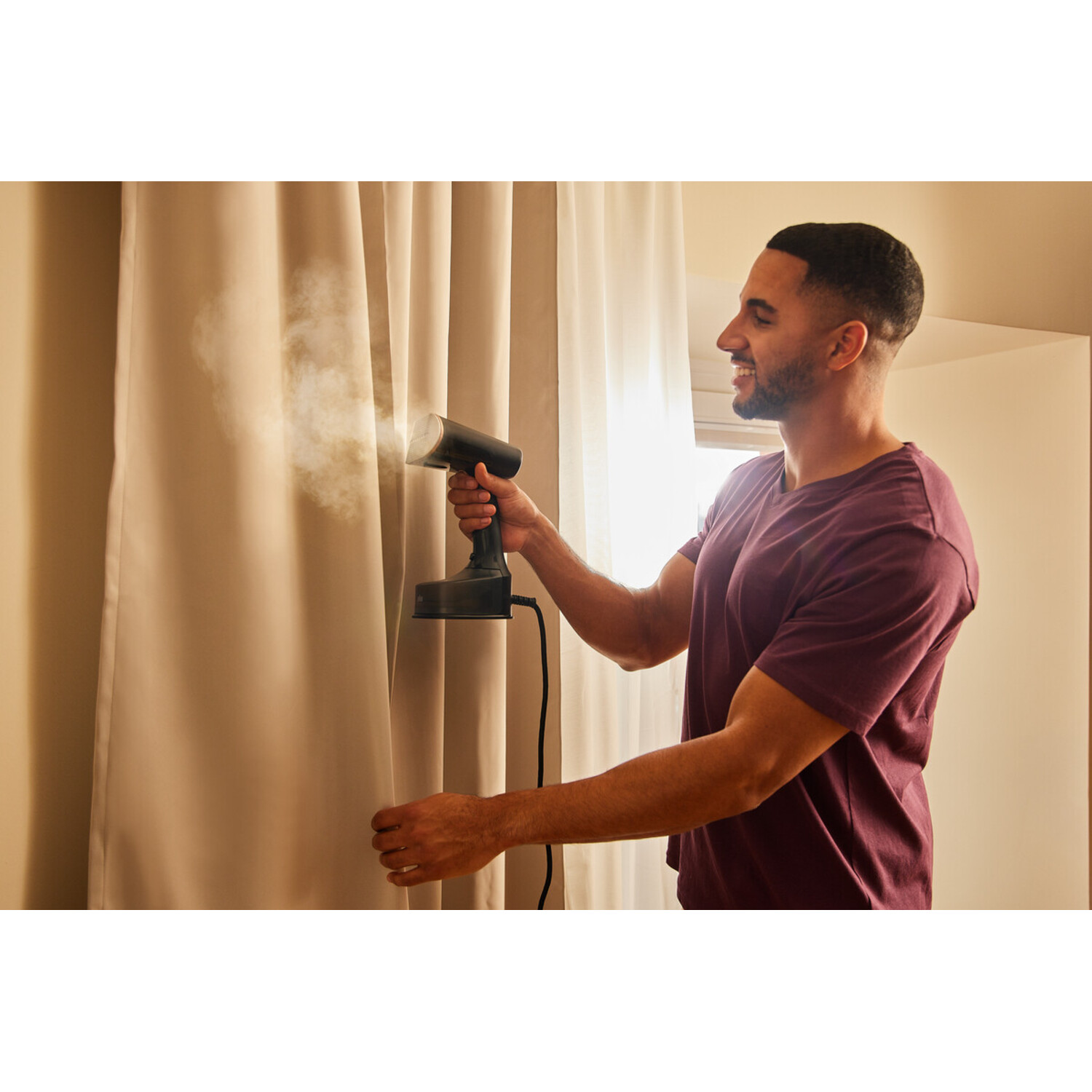 Man steaming a curtain with a handheld steamer.