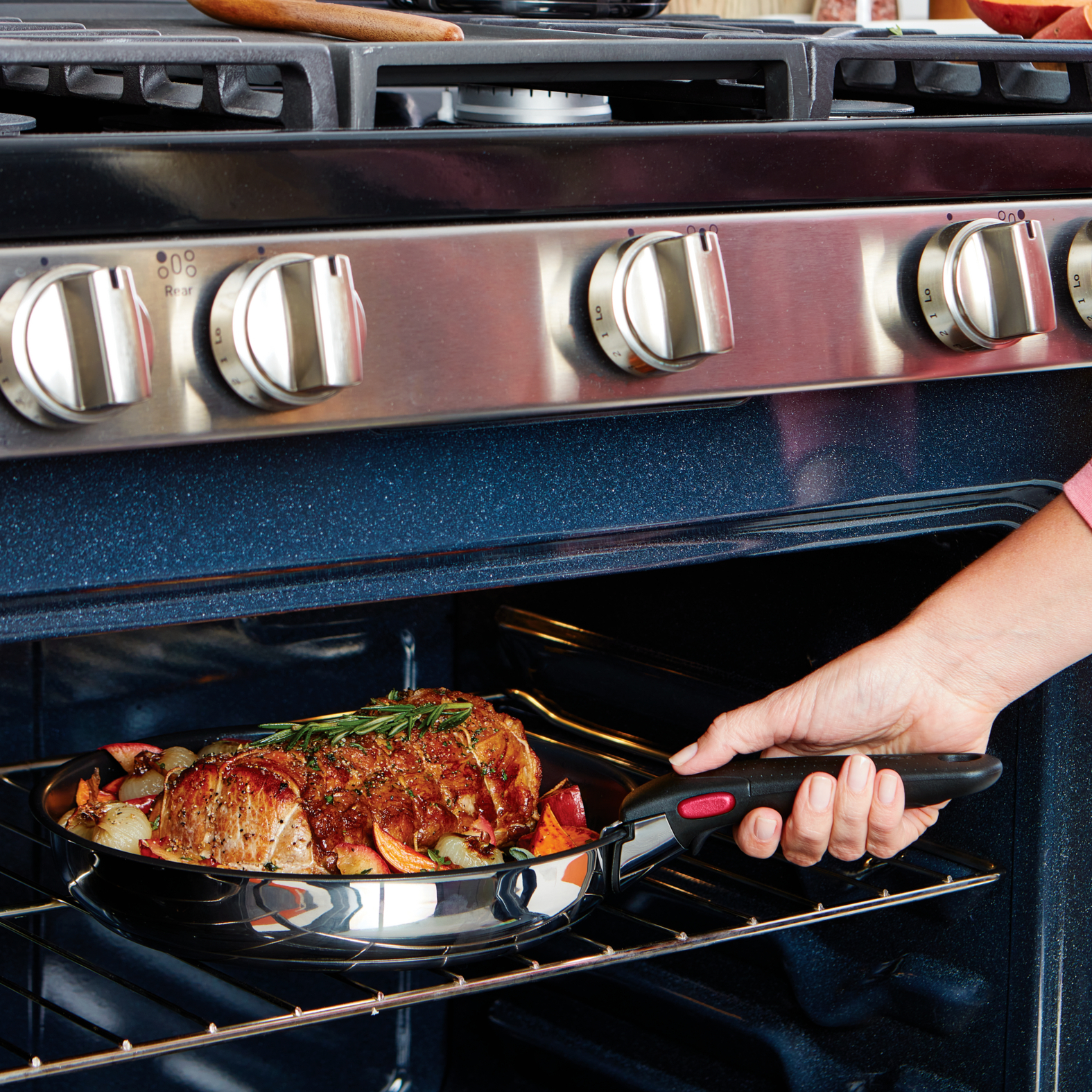 Ręka wyciąga patelnię z ugotowanym jedzeniem z piekarnika. Jedzenie jest na okrągłej patelni.