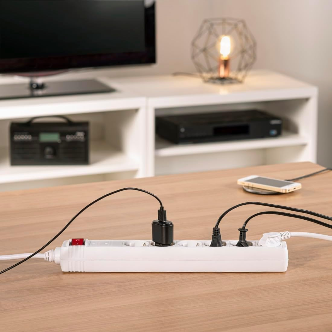 Una regleta blanca con varios enchufes conectados, sobre una mesa de madera.