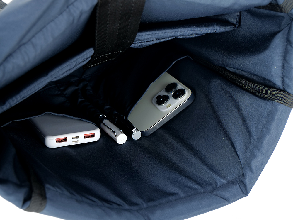 Egy sötétkék táskában egy telefon, toll és power bank látható. A tárgyak egy zsebben vannak.